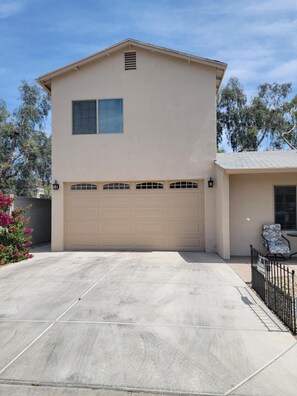 A two-story house with a beige exterior, a garage, and a small patio area with a chair.