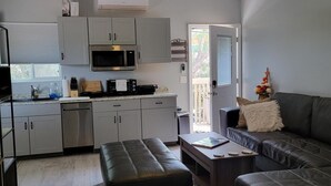 A modern kitchen with grey cabinets, a microwave, and a built-in oven. There is a dining area with a black leather couch and a small table.