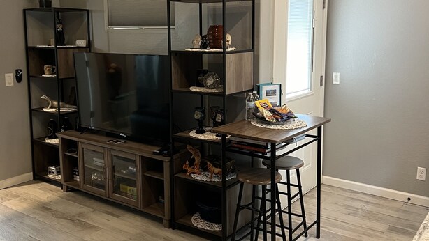 A living room with a flat-screen TV, wooden entertainment center, and a dining area with a bar stool.