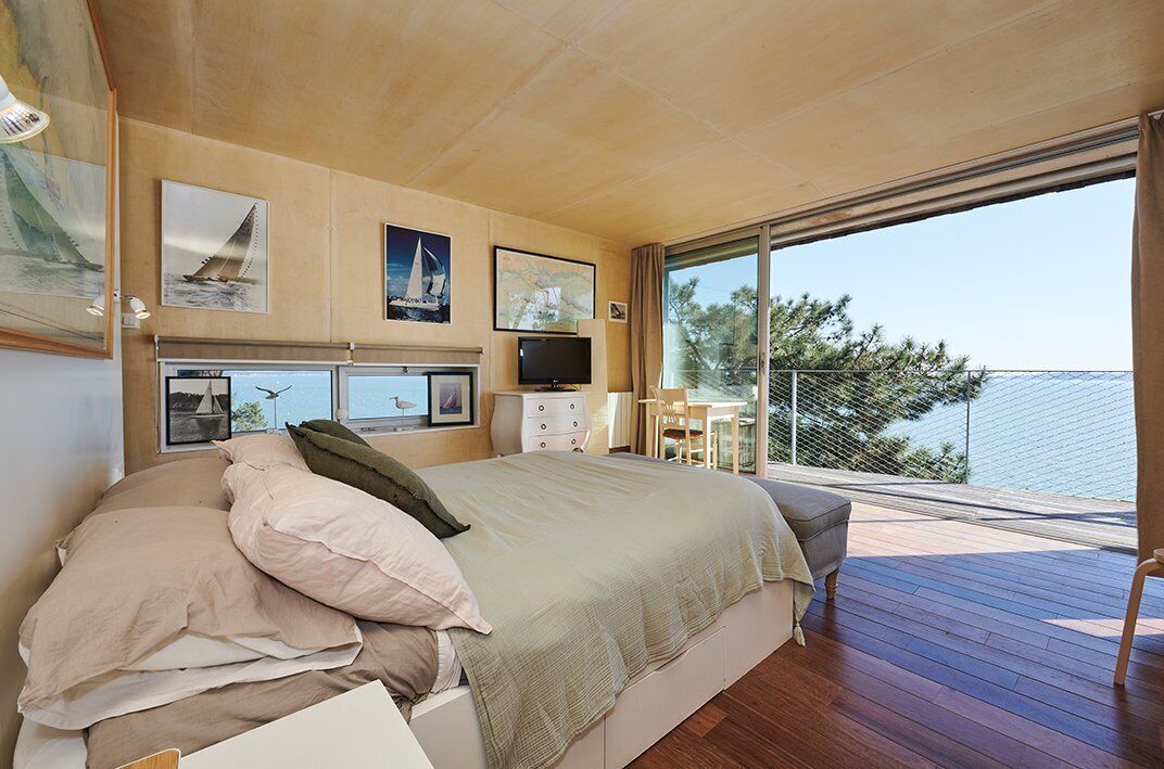 A bedroom with a large bed, a TV, and a balcony with a view of the sea.