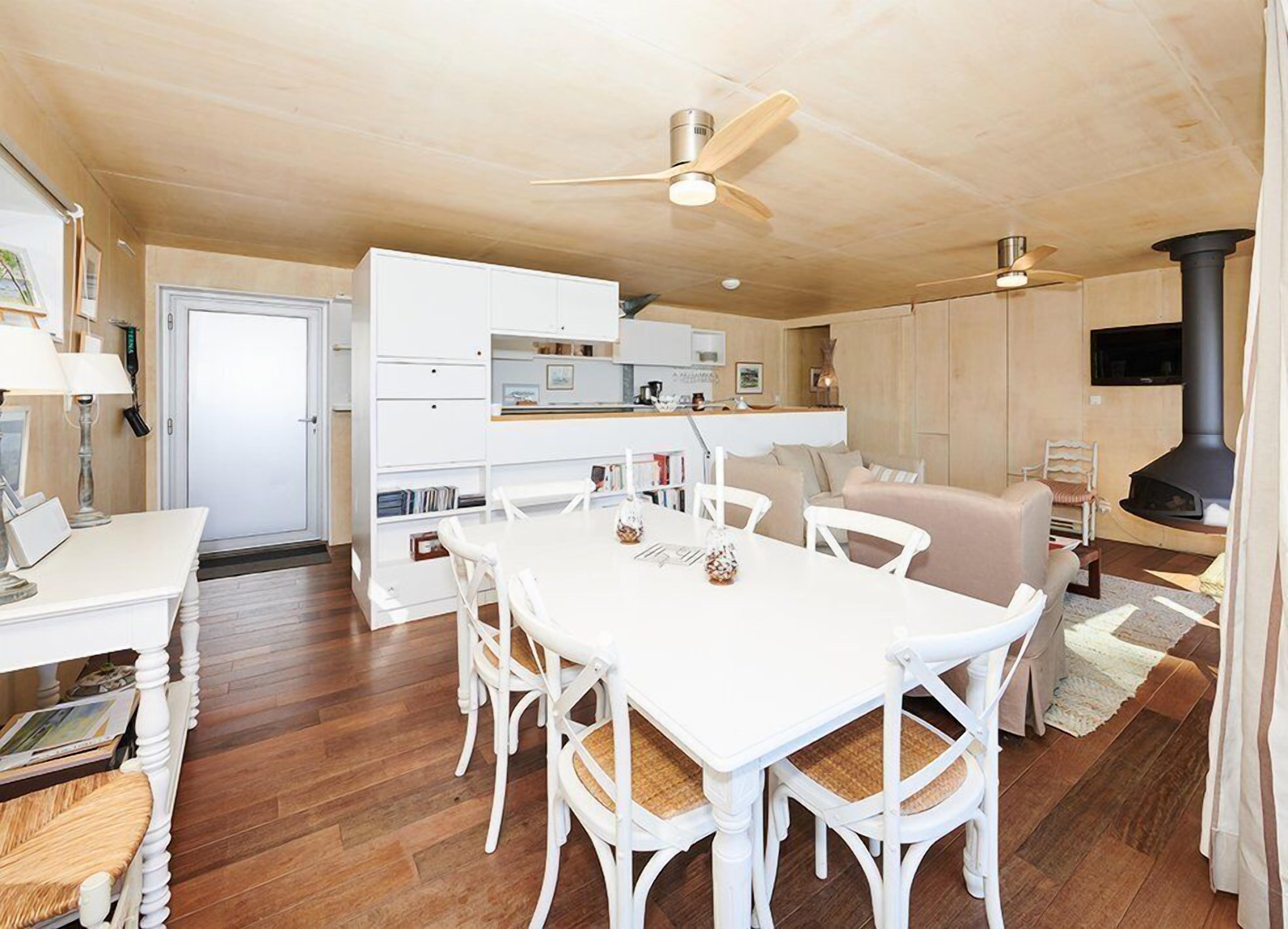 A modern kitchen with white cabinetry, a dining table with white chairs, and a wood-burning stove.