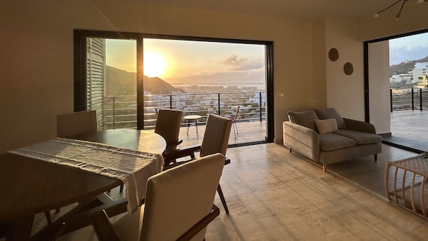 A modern living room with a dining area, large sliding glass doors, and a city view.