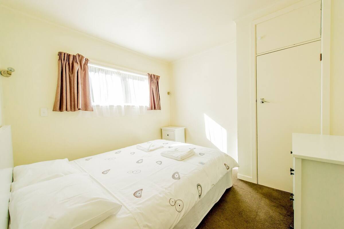 Une chambre à coucher avec un lit, une table de chevet, une fenêtre avec des rideaux et une porte.