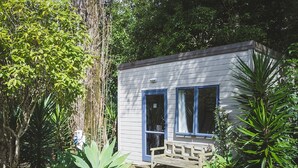 A small cabin with a deck, surrounded by dense greenery. - Touchwood Motor Inn (Auckland)