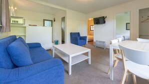 A modern, well-lit living room with a blue sofa, a white coffee table, and a dining area with a white table and wooden chairs. - Touchwood Motor Inn (Auckland)