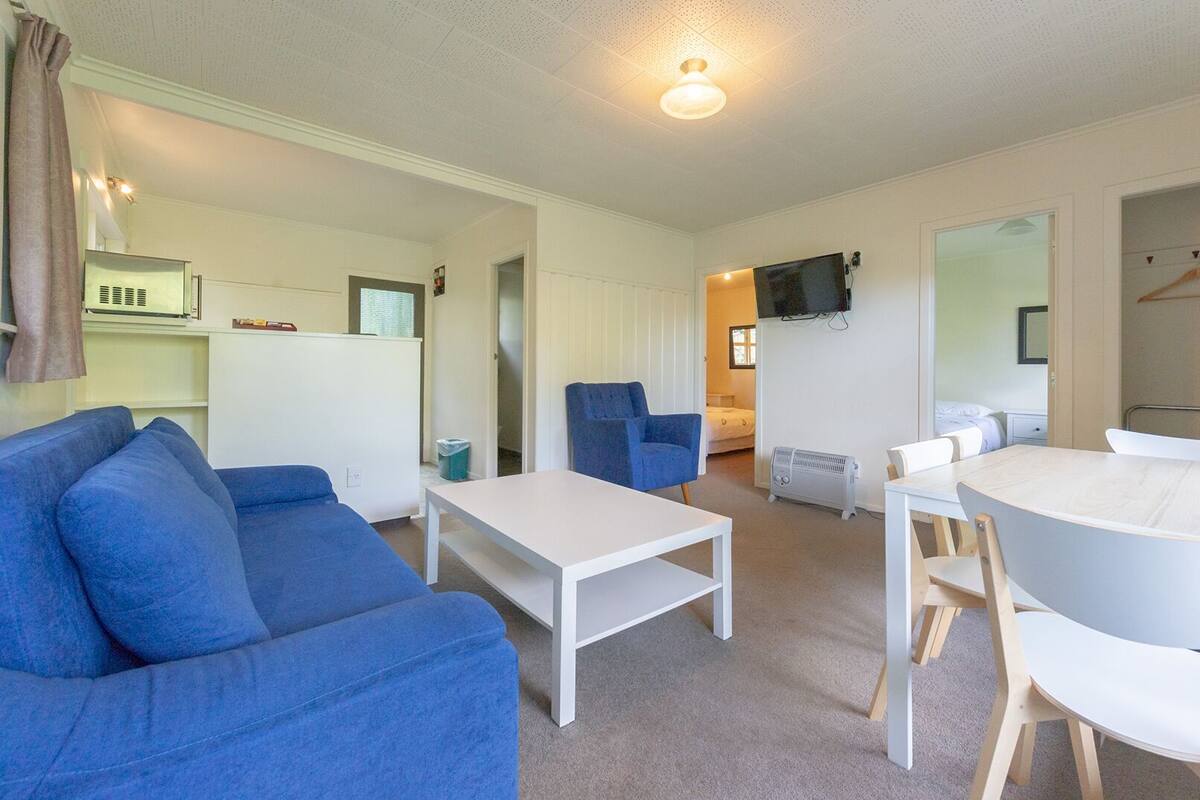 Un salon moderne et bien éclairé, avec un canapé bleu, une table basse blanche et un coin repas comprenant une table blanche et des chaises en bois.