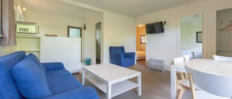 A modern, well-lit living room with a blue sofa, a white coffee table, and a dining area with a white table and wooden chairs.