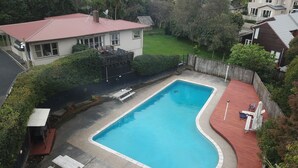 A rectangular swimming pool with a curved edge, surrounded by a wooden deck and a red border. - Touchwood Motor Inn (Auckland)