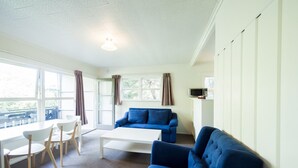 A modern living room with a blue sofa, white coffee table, and a dining area with a white table and chairs. - Touchwood Motor Inn (Auckland)