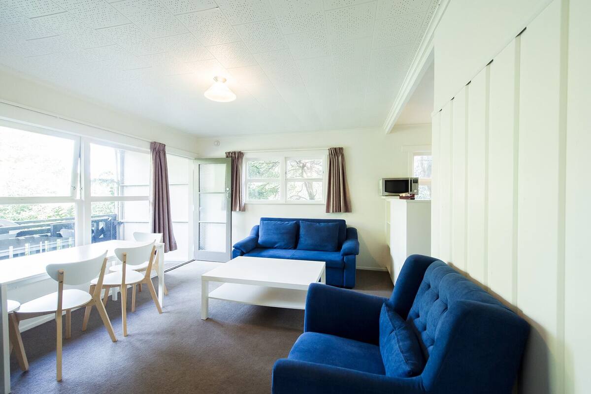 Un salon moderne avec un canapé bleu, une table basse blanche et un coin repas comprenant une table et des chaises blanches.