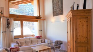 Un salon confortable avec un canapé, une table basse et un fauteuil. Il y a une fenêtre avec des rideaux, un meuble en bois et un luminaire fixé au mur.