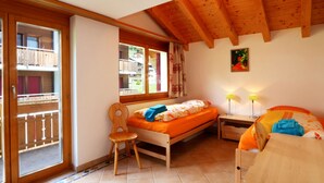 Une chambre à coucher avec un lit en bois, une chaise, une table de chevet et une fenêtre donnant sur un balcon.