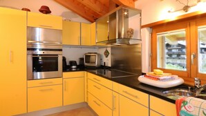 Une cuisine avec des meubles de couleur jaune, des appareils électroménagers en acier inoxydable et une fenêtre donnant sur des immeubles.