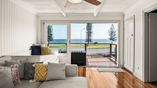 A room with a wooden floor, a ceiling fan, a sofa with cushions, and a view of the sea through large windows. - Stunning vacation rental offering unique city and beach views (Clontarf)