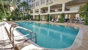A swimming pool with a tiled deck, surrounded by palm trees and lounge chairs.