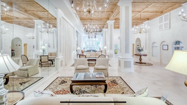 A spacious, elegantly furnished lounge with high ceilings, chandeliers, and a central seating area.