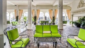 A spacious indoor patio with green cushioned seating, a patterned coffee table, and potted plants.