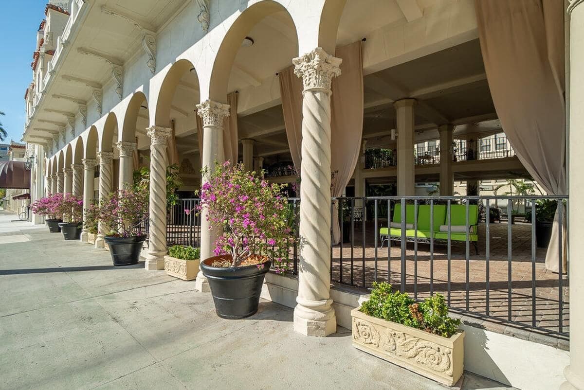 Un bâtiment doté d’une série d’arches et de colonnes, d’un espace extérieur aménagé pour s’asseoir et de plantes en pot.