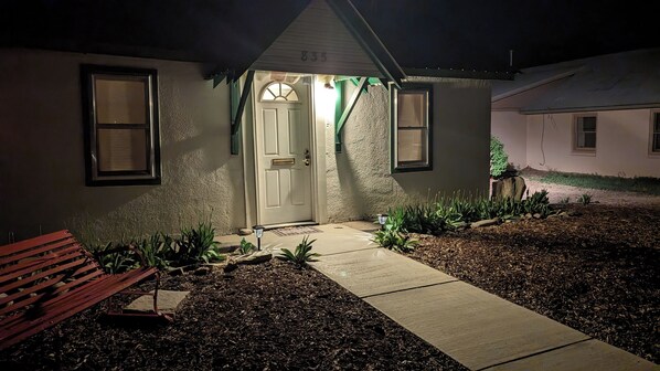 A house with a front door, two windows, a bench, and a pathway leading to the door.