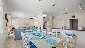 A dining area with a white table and blue cushioned chairs, a kitchen in the background, and a ceiling fan. - Magical getaway for the entire Family. (Davenport)
