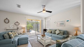 A living room with two blue sofas, a coffee table, and a ceiling fan. There are clocks on the wall and a window with blinds. - Magical getaway for the entire Family. (Davenport)
