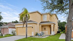 A two-story residential house with a garage, a small front yard with a palm tree, and a clear sky. - Magical getaway for the entire Family. (Davenport)