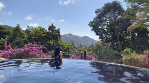Una persona sentada en una piscina infinita con un paisaje montañoso al fondo.