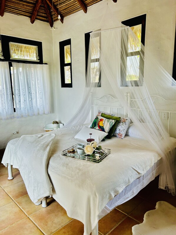 Un dormitorio con cama a dosel, una mesita de noche, una bandeja con té y pastelería, y una ventana con cortinas.