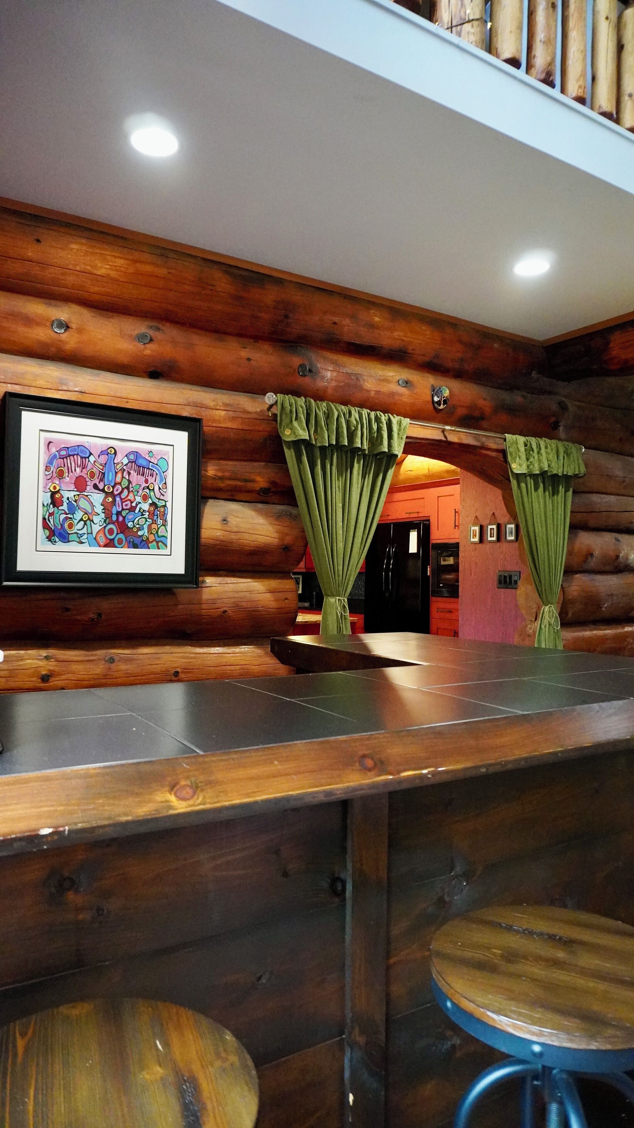Un interno in legno con angolo bar, opere d'arte incorniciate e tende verdi.