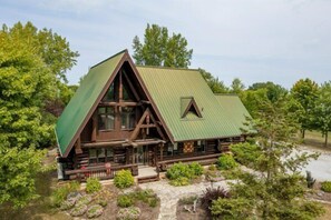 A log cabin with a green roof, surrounded by lush greenery and a stone pathway. - The Lodge at Lakeshore (Emeryville)