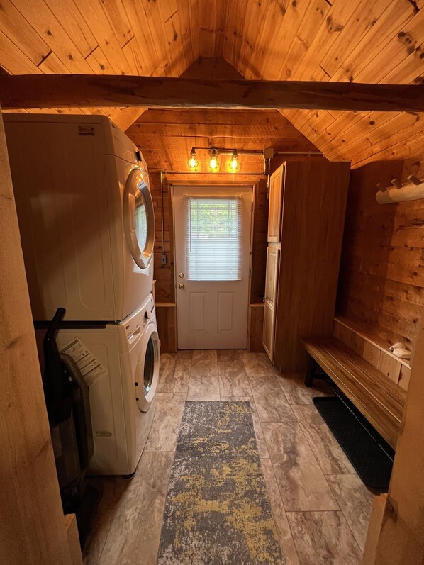 A compact laundry room with a washing machine, dryer, and a bench. - Waterfall Cabin - Pictured Rocks Lodging (Munising)