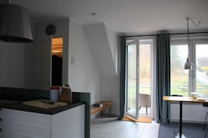 Uma cozinha moderna com uma ilha grande, uma sala de jantar com mesa e cadeiras, e uma porta de vidro deslizante para uma varanda.