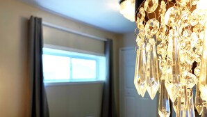 Hotellihuone, jossa on sänky, ikkuna verhoilla ja kristallikoristeilla varustettu kattokruunu.