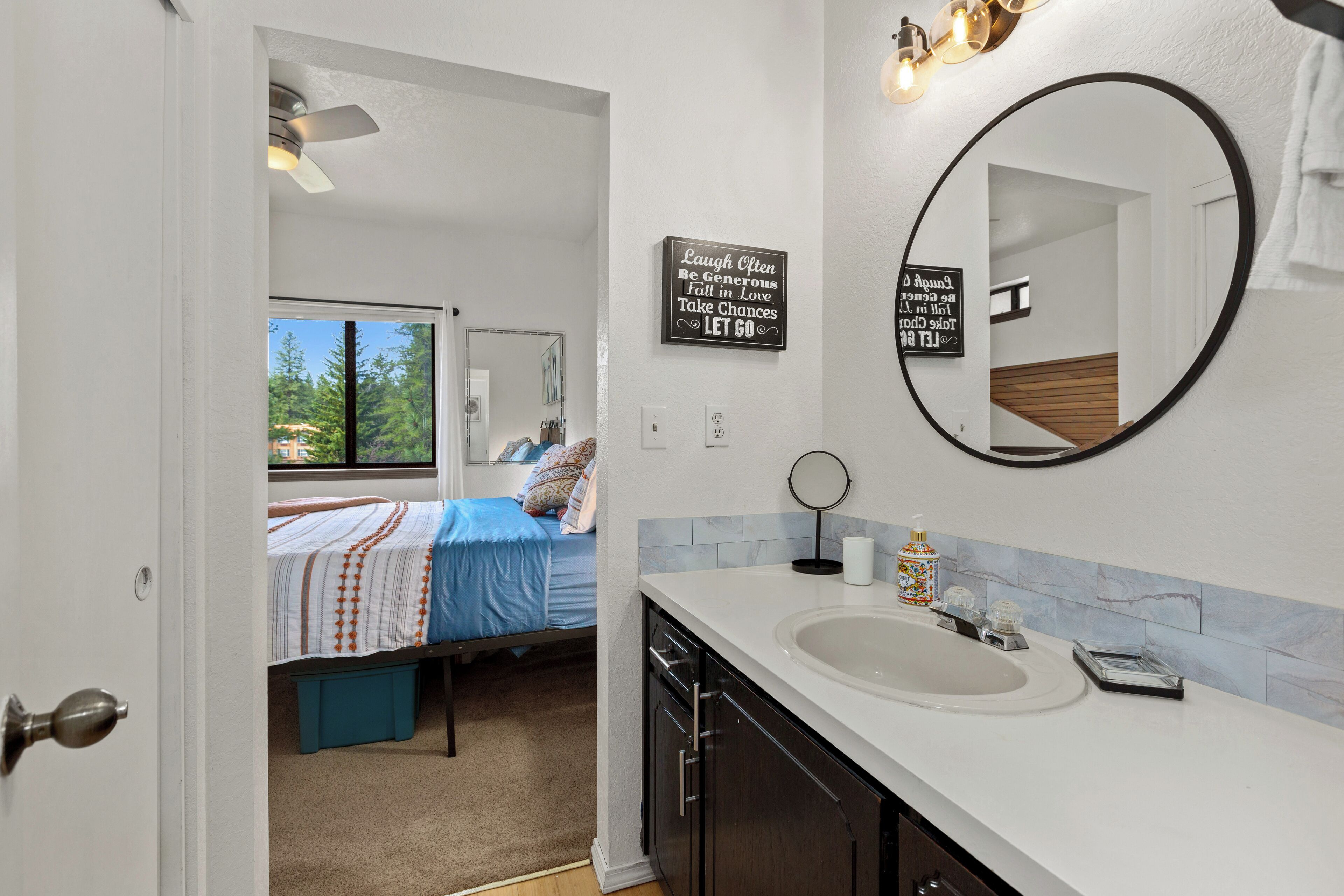 A bedroom with a bed, a bathroom with a sink and mirror, and a motivational quote on the wall.