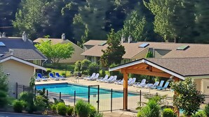 Une piscine entourée de chaises longues et d’un kiosque, avec des maisons et des arbres en arrière-plan.