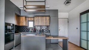 Une cuisine moderne dotée d’un îlot central, de meubles de rangement aux couleurs sombres et d’un plan de travail en bois.