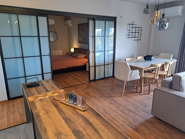 Een modern interieur met een houten eettafel, een bank en een bed met een schuifdeur van glas.