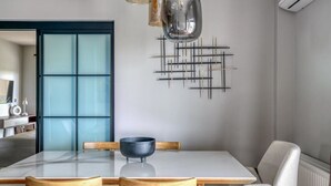 Un espace repas moderne avec une table blanche, deux chaises en bois, un bol noir et une œuvre d’art géométrique accrochée au mur.