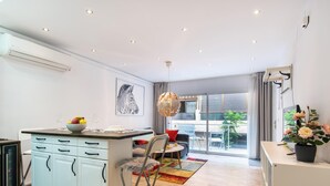 A modern kitchen with a central island, a dining area with a round table and chairs, and a large window offering a view of the outdoors. - 2nd line Boliches Beach Apartment (FUENGIROLA)