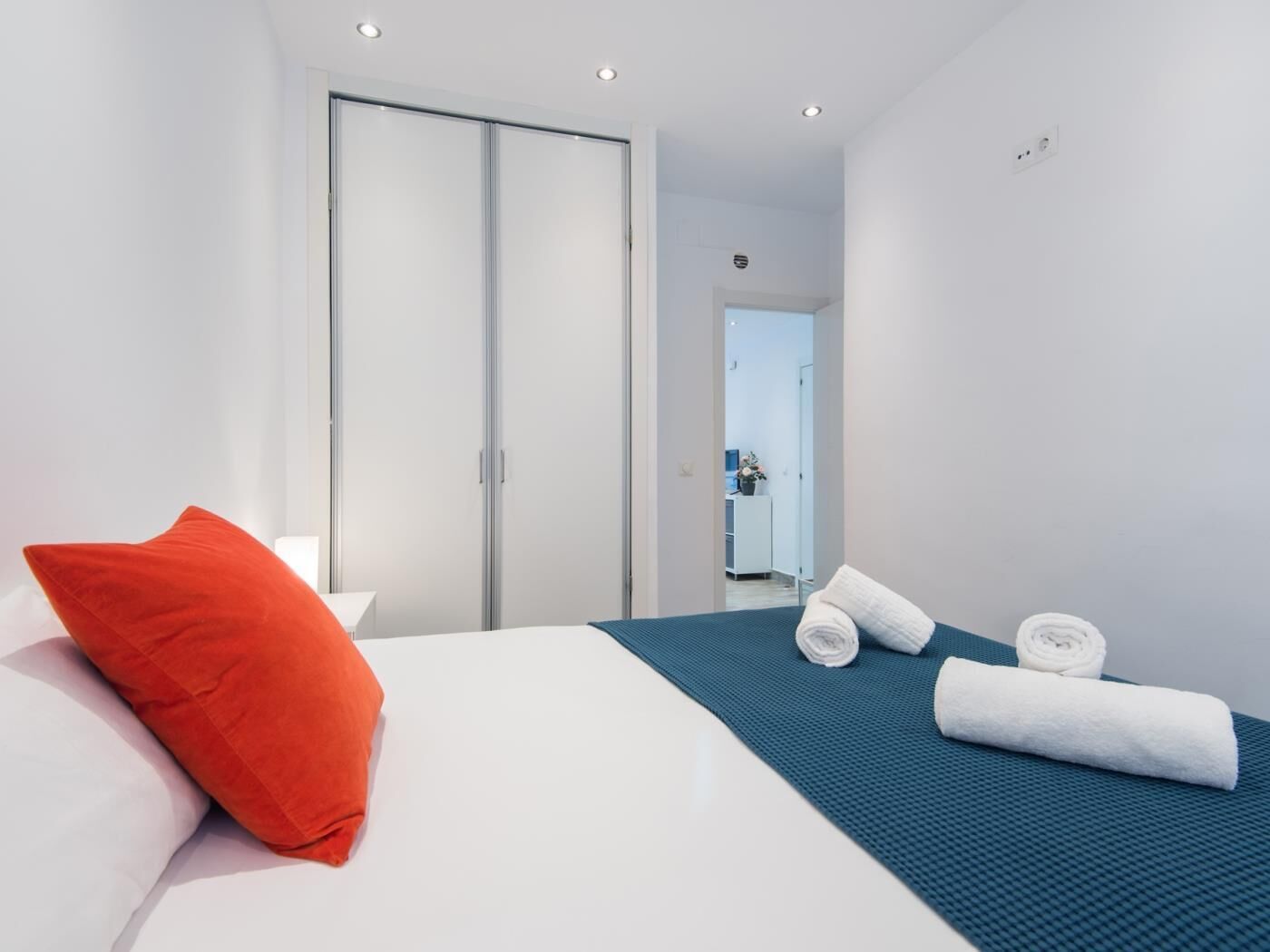 A modern hotel room with a bed, a red pillow, a blue bedspread, and a towel.