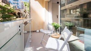 A balcony with a glass railing, two white chairs, a small table with a vase of flowers, and a view of neighboring buildings. - 2nd line Boliches Beach Apartment (FUENGIROLA)