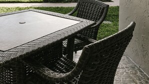 Une terrasse extérieure avec une table et des chaises en osier, une pelouse et un bâtiment en arrière-plan.