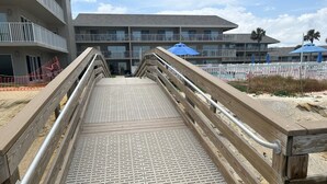 Une promenade en bois mène à un bâtiment doté de nombreux balcons et d’un espace piscine.