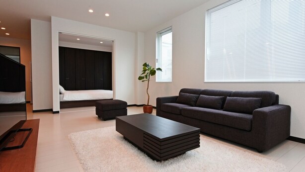 A modern living room with a dark sofa, a coffee table, and a large window with blinds. - TEINE HOTEL (Sapporo)