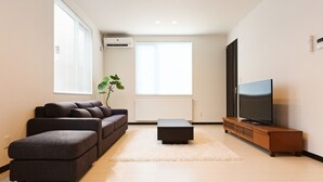 A modern living room with a sofa, ottoman, TV, and a plant. - TEINE HOTEL (Sapporo)