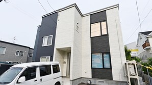 A modern two-story residential building with a white and dark grey facade, a visible garage door, and a parked white van in front. - TEINE HOTEL (Sapporo)