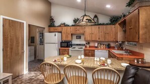Une cuisine compacte avec des meubles en bois, un îlot central doté de chaises, un réfrigérateur, un four à micro-ondes, une cuisinière et un évier.