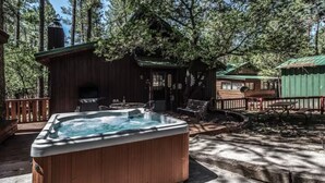 Un bain à remous en bois, situé dans une zone boisée, avec un chalet et du mobilier d’extérieur.
