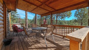 Een houten terras met een tafel en stoelen, een Amerikaanse vlag en uitzicht op bomen.