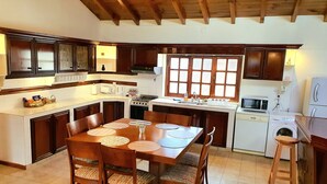 Una cocina con armarios de madera, una mesa de comedor con sillas, un ventanal y una lavadora.